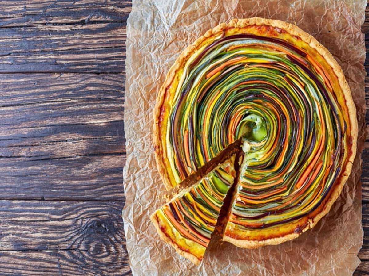 vegetable Spiral tart with zucchini, eggplant, carrot slices with ricotta cheese and egg filling cut in slices on a paper, view from above, copy space